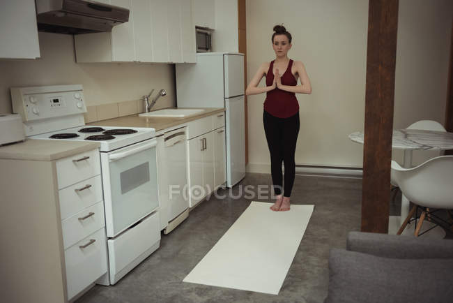 Mujer realizando yoga en cocina en casa - foto de stock