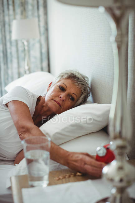 Senior woman lying on bed and turning off an alarm clock in bedroom at home — Stock Photo