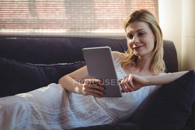 Beautiful woman lying on sofa and using digital table in living room at home — Stock Photo