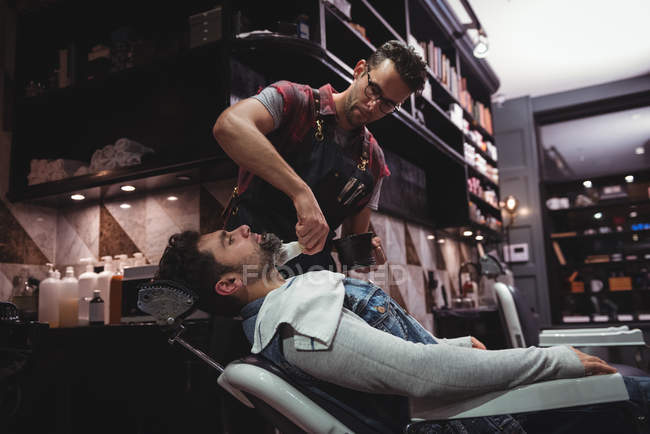 Barbeiro aplicando creme na barba do cliente na barbearia — Fotografia de Stock
