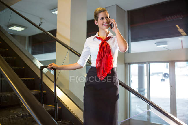 Equipe feminina com bagagem conversando no telefone celular na escada rolante no aeroporto — Fotografia de Stock