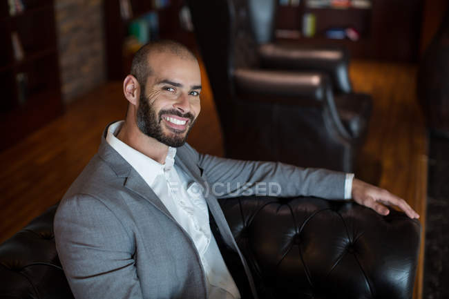 Портрет улыбающегося бизнесмена, сидящего на диване в зале ожидания терминала аэропорта — стоковое фото