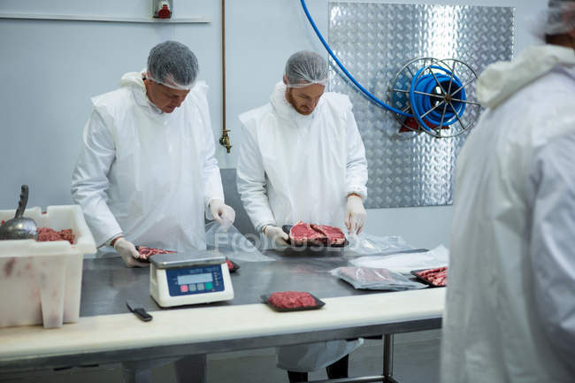 Açougueiros que pesam embalagens de carne na fábrica de carne — Fotografia de Stock