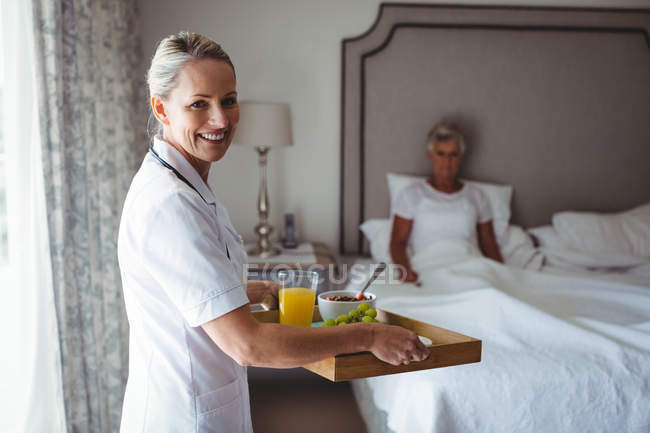Portrait of doctor holding breakfast for patient sitting in background at home — Stock Photo