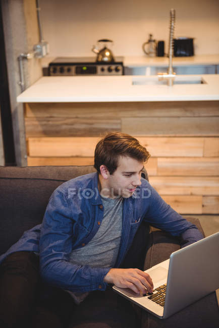 Мужчина сидит на диване, используя ноутбук в гостиной на дому — стоковое фото