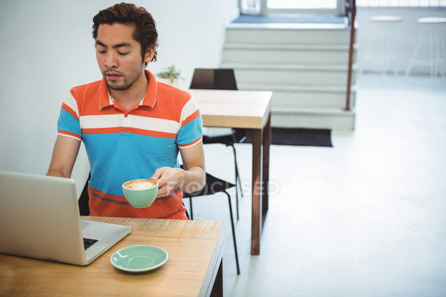 Людина використовує ноутбук, маючи чашку кави в кав'ярні — стокове фото