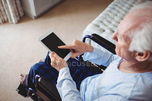 Старший мужчина сидит на инвалидной коляске и использует цифровой планшет дома — стоковое фото