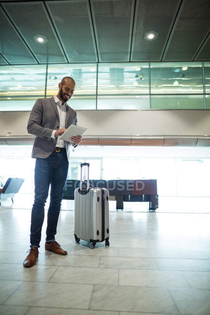Улыбающийся бизнесмен, использующий цифровой планшет в зоне ожидания в терминале аэропорта — стоковое фото