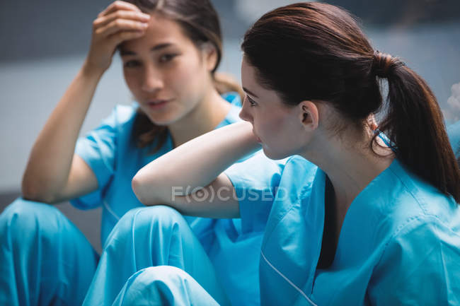 Грустные медсестры сидят на коридоре в больнице — стоковое фото