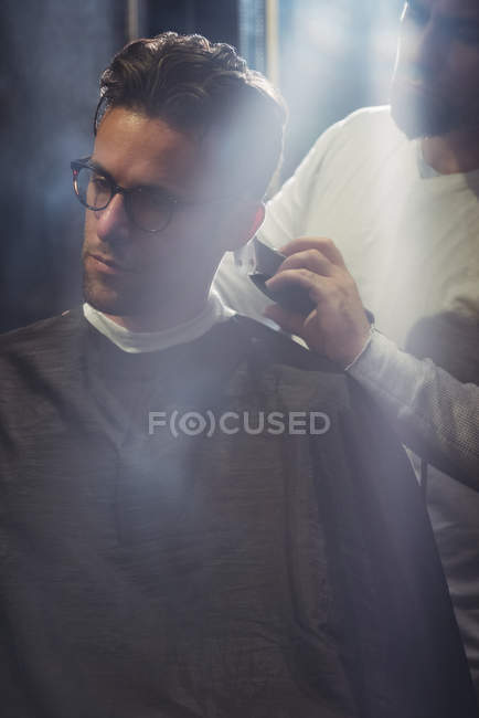 Homem recebendo cabelo aparado por barbeiro com aparador na barbearia — Fotografia de Stock
