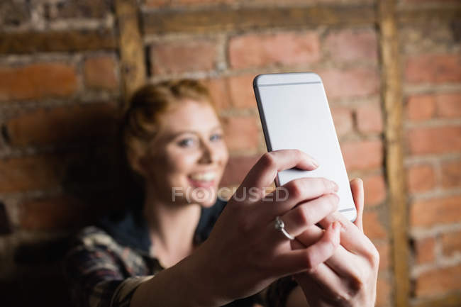 Femme debout contre un mur de briques et prenant un selfie sur son téléphone portable — Photo de stock