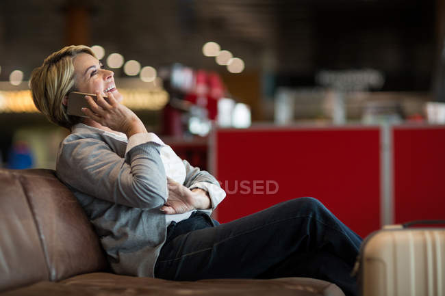 Businesswoman talking on mobile phone in waiting area at airport terminal — Stock Photo