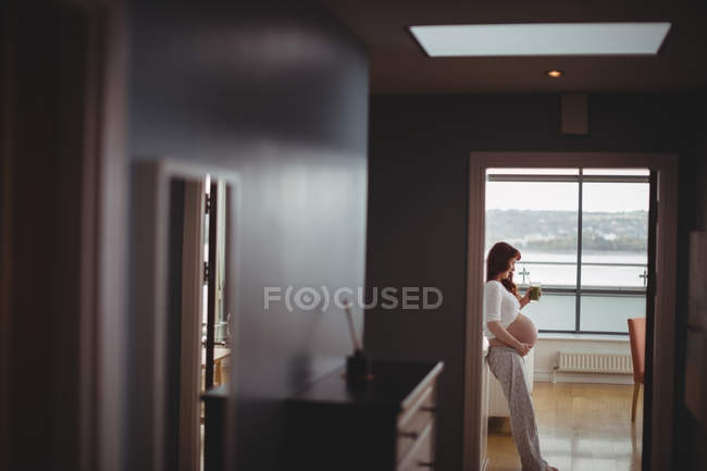 Femme enceinte réfléchie tenant un verre de jus à la maison — Photo de stock