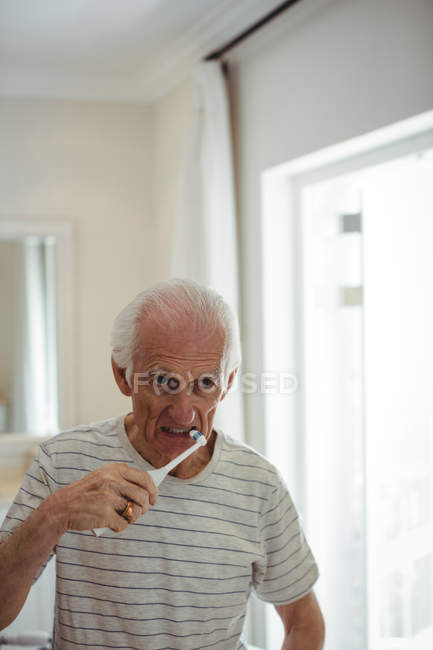 Hombre mayor cepillándose los dientes en el baño - foto de stock