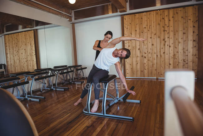 Entrenador ayudando a la mujer mientras practica pilates en el gimnasio - foto de stock