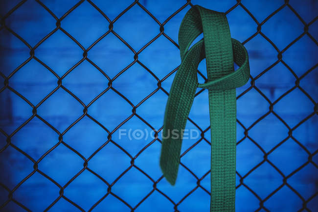 Close-up de cinto verde karatê pendurado na cerca de malha de arame no estúdio de fitness — Fotografia de Stock