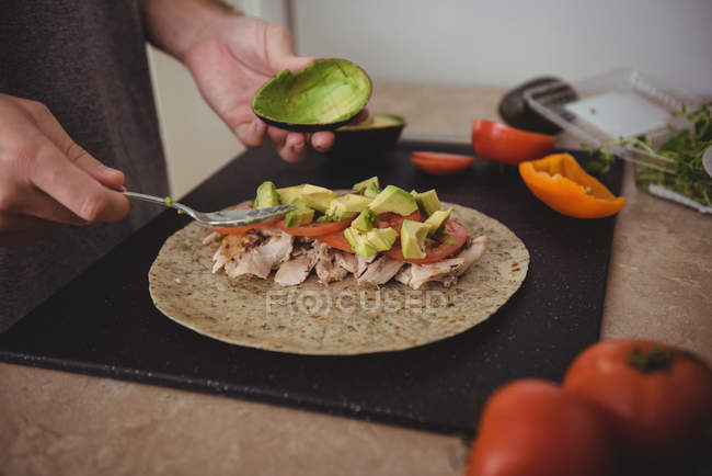 Sección media del hombre preparando un burrito en la cocina en casa - foto de stock