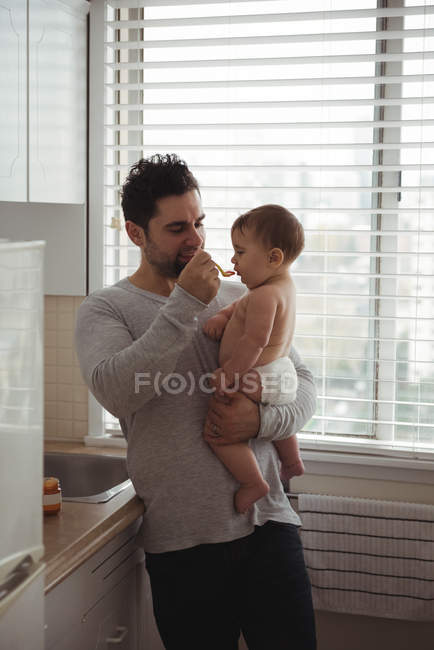 Pai alimentando bebê filho na cozinha em casa — Fotografia de Stock
