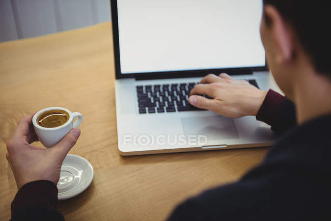 Людина використовує ноутбук, маючи каву в кав'ярні — стокове фото
