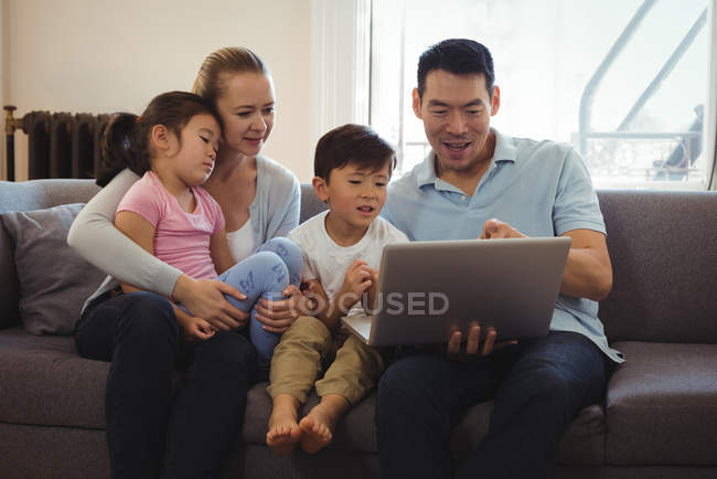 Sonrientes padres e hijos usando el portátil en la sala de estar en casa - foto de stock