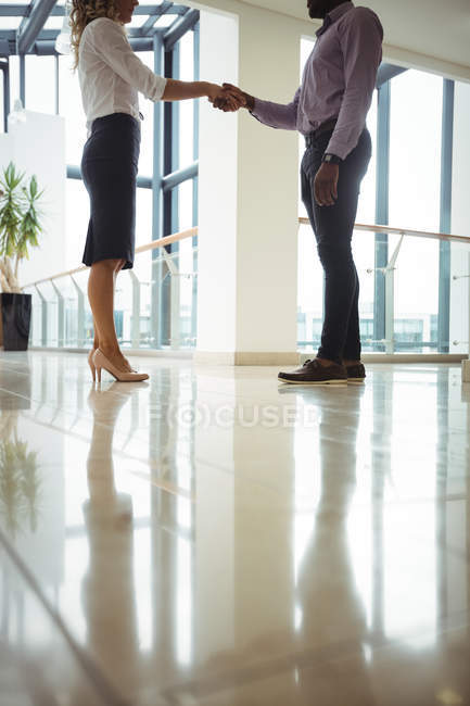 Ejecutivos de negocios estrechando las manos en el pasillo de la oficina - foto de stock