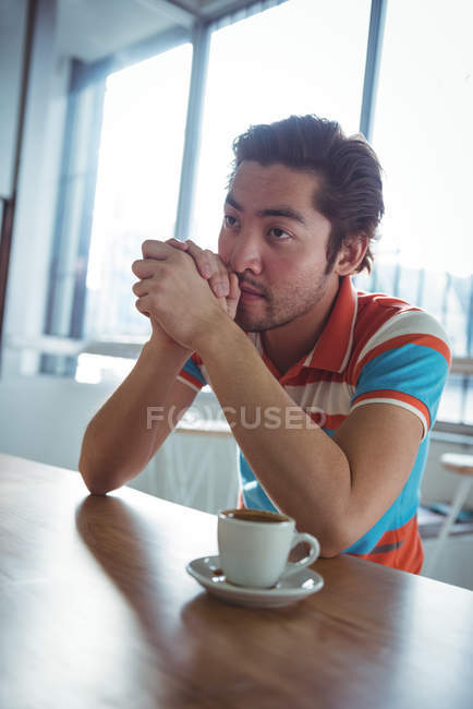 Вдумчивый человек сидит с чашкой кофе на столе в кафе — стоковое фото