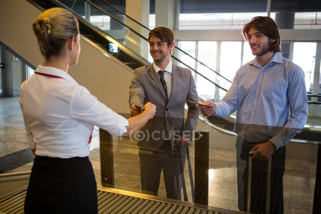 Female staff checking boarding pass of passengers at check-in counter in airport — Stock Photo
