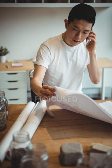 Geschäftsführender Angestellter telefoniert mit dem Handy, während er sich im Büro den Bauplan ansieht — Stockfoto