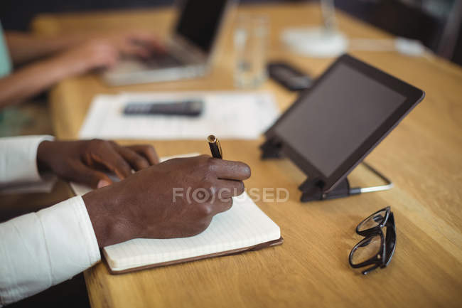 Primer plano del hombre de negocios escribiendo en un diario en el escritorio en la oficina - foto de stock