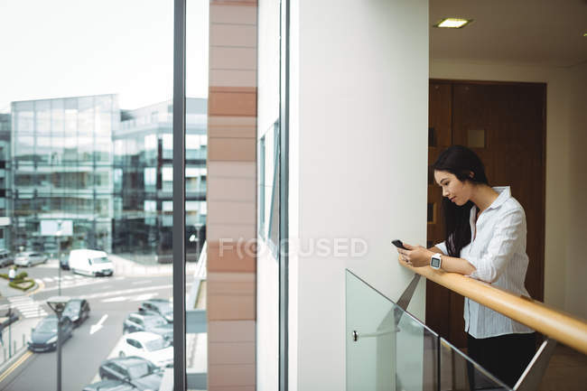 Seitenansicht einer Geschäftsfrau, die ihr Handy auf dem Bürobalkon benutzt — Stockfoto