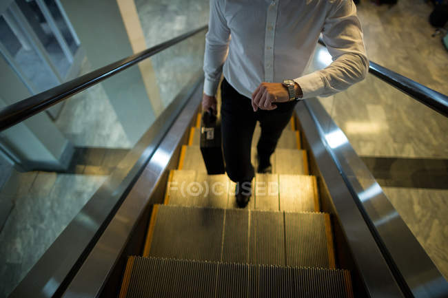 Viajeros buscando tiempo mientras camina en escaleras mecánicas en el aeropuerto - foto de stock