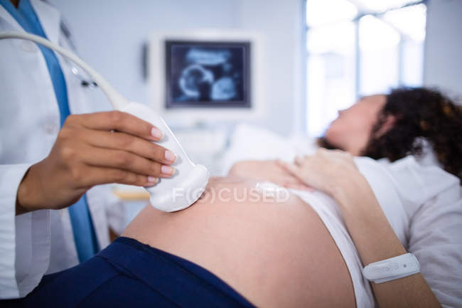 Sección media del médico haciendo ecografía para la mujer embarazada en el hospital - foto de stock