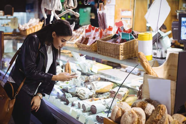 Mujer usando el teléfono móvil mientras mira la pantalla de comida en el supermercado - foto de stock