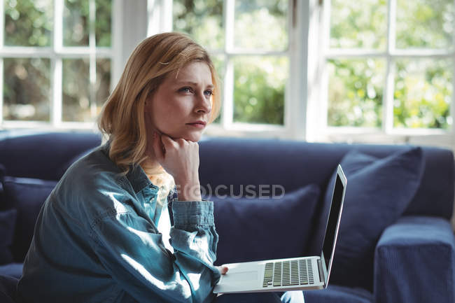 Femme réfléchie utilisant un ordinateur portable dans le salon à la maison — Photo de stock