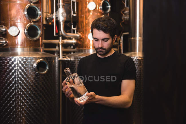 Homme examinant une bouteille d'alcool dans une usine de bière — Photo de stock