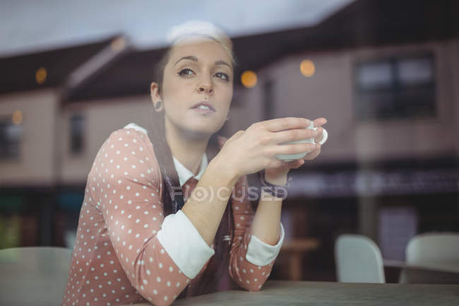 Задумчивая женщина смотрит в окно, выпивая чашку кофе в кафе — стоковое фото