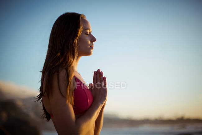 Beautiful woman meditating on beach at dusk — Stock Photo