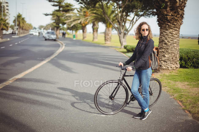 Mulher de pé com bicicleta na estrada — Fotografia de Stock