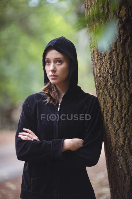 Задумчивая женщина, стоящая в лесу с руками — стоковое фото