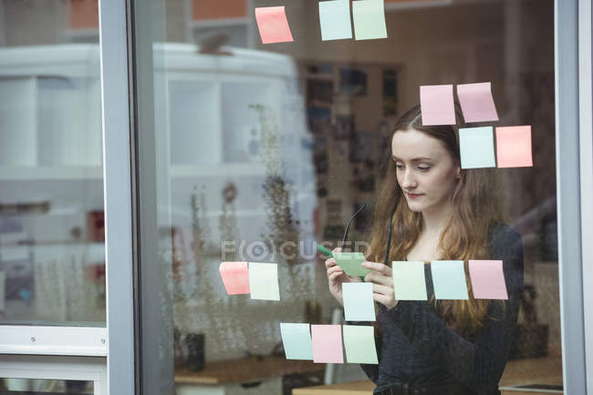 Escritura ejecutiva femenina en notas adhesivas en la oficina - foto de stock