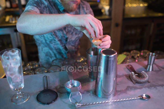 Bartender adding egg yolk while preparing drink at counter in bar — Stock Photo