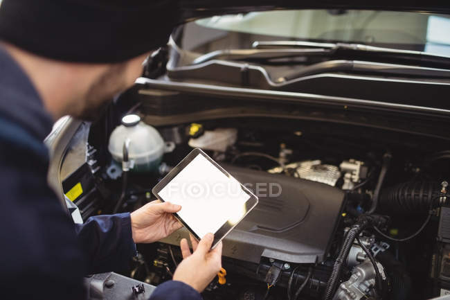 Mechanic using digital tablet on car in repair garage — Stock Photo