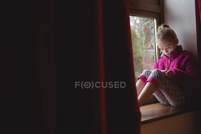Chica sentada en el alféizar de la ventana y el uso de tableta digital en casa - foto de stock