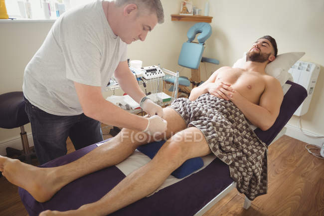 Fisioterapeuta realizando agujas secas en la rodilla del paciente masculino en la clínica - foto de stock