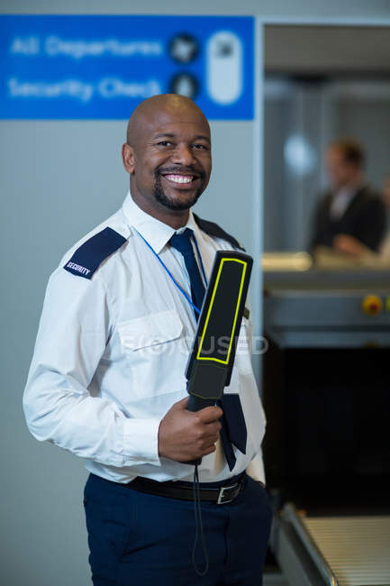 Portrait of smiling airport security officer holding metal detector in airport terminal — Stock Photo