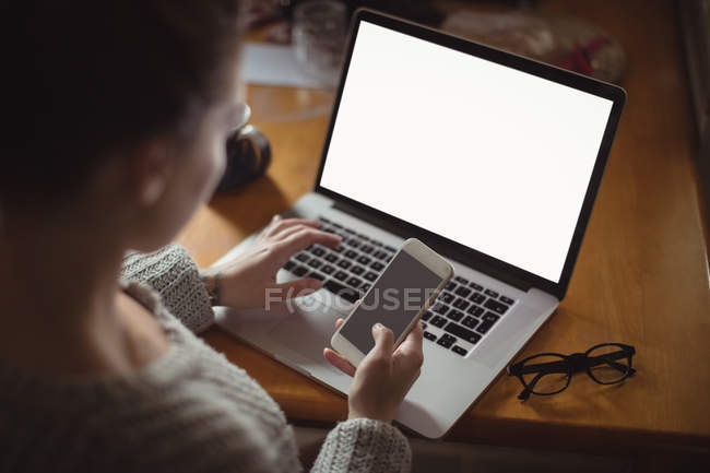 Жінка використовує мобільний телефон і ноутбук на столі вдома — стокове фото