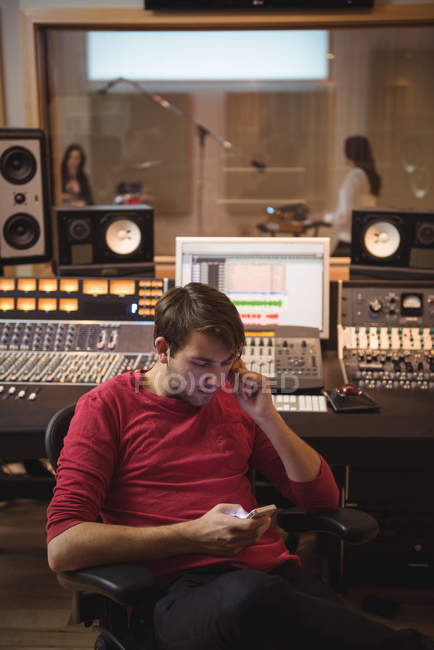 Engenheiro de áudio usando smartphone perto do mixer de som no estúdio de gravação — Fotografia de Stock