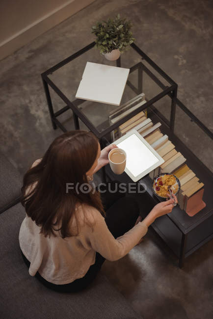 Женщина с цифровым планшетом завтракает в гостиной дома — стоковое фото