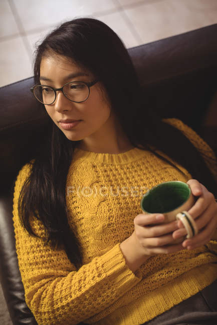 Задумчивая женщина сидит и пьет кофе на диване дома — стоковое фото