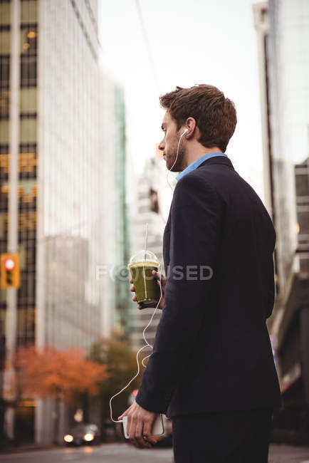Geschäftsmann hört Musik auf Handy, während er auf der Straße steht — Stockfoto